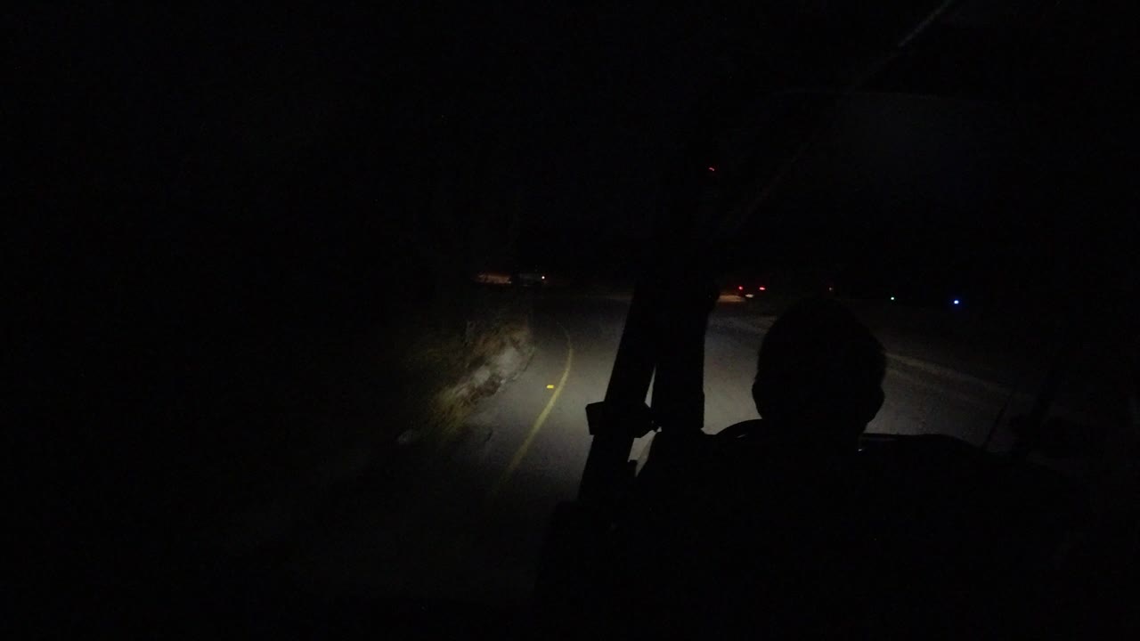 Dark windshield view of a road lit by headlights
