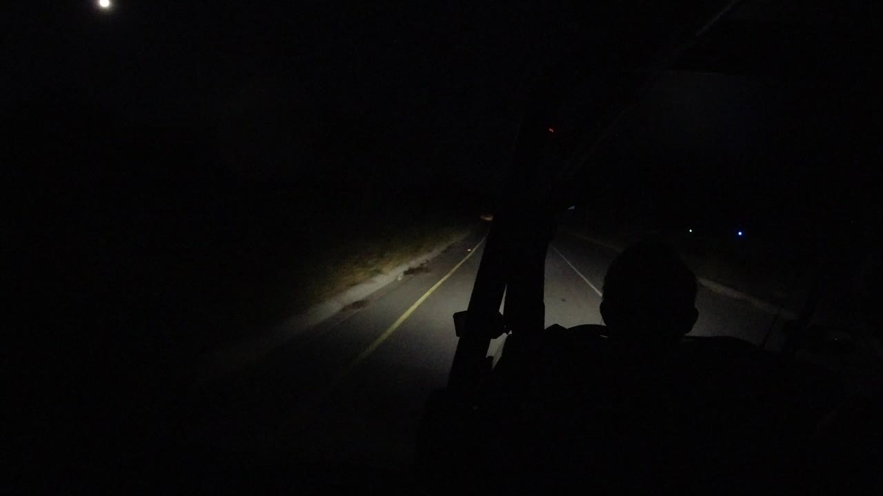Dark road lit by vehicle headlights at night.
