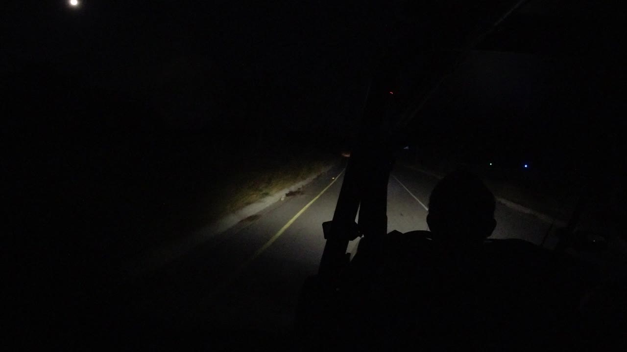 A forward-facing night view in Los Cabos, Mexico shows the empty road receding ahead, with the brightest light falling on the left shoulder and no recognizable people visible.