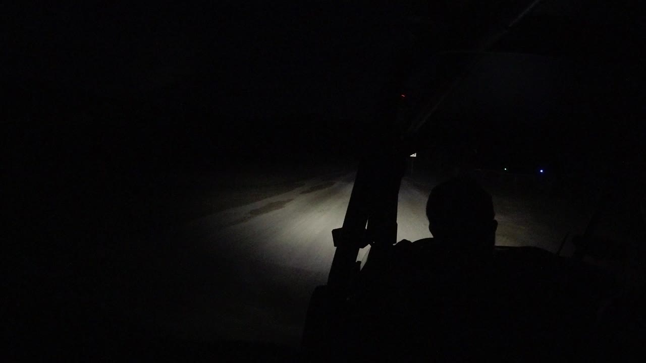 Dark vehicle interior with a driver silhouette and headlights on a road.