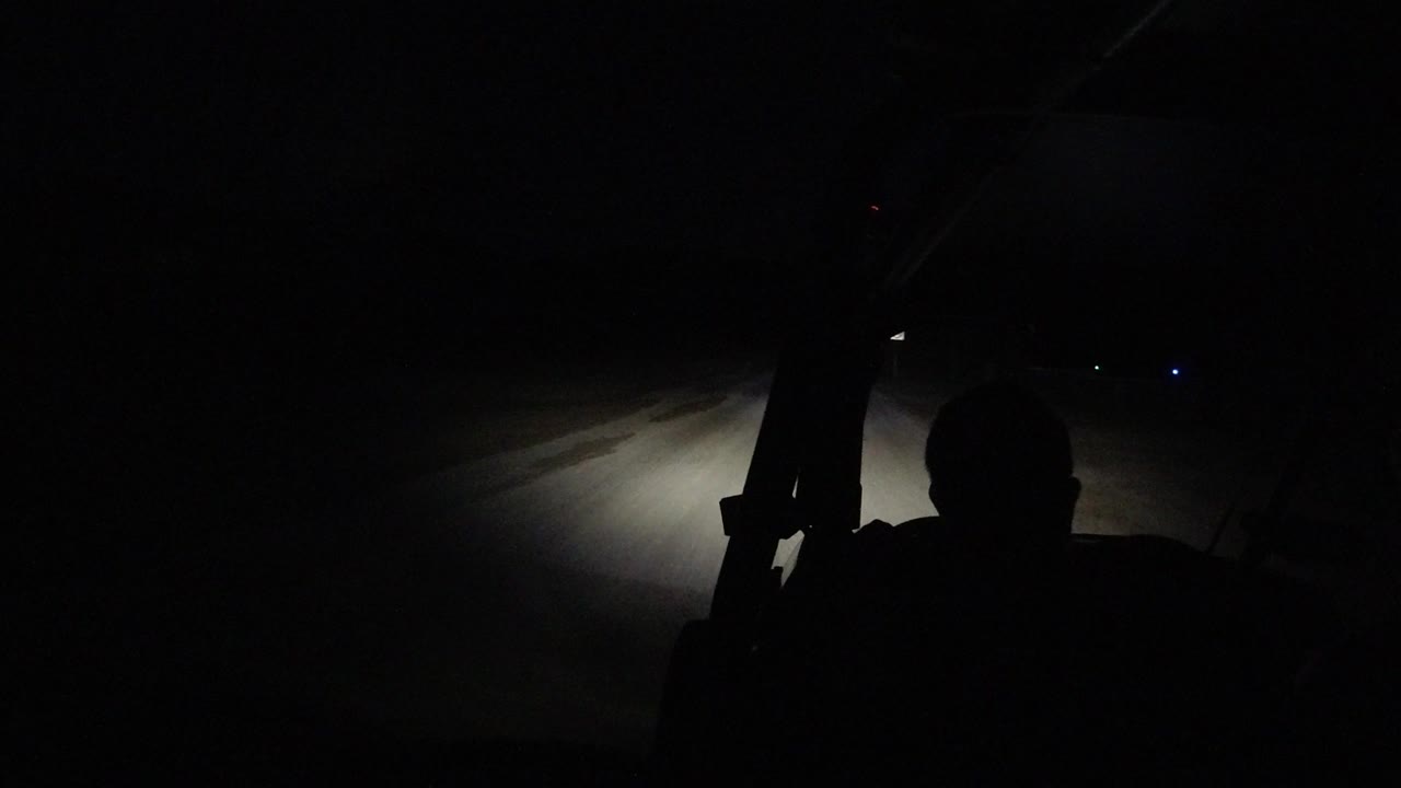 At 0:01 in Los Cabos, Mexico, the silhouetted driver remains in the foreground as the headlight glow falls slightly left across the road surface.