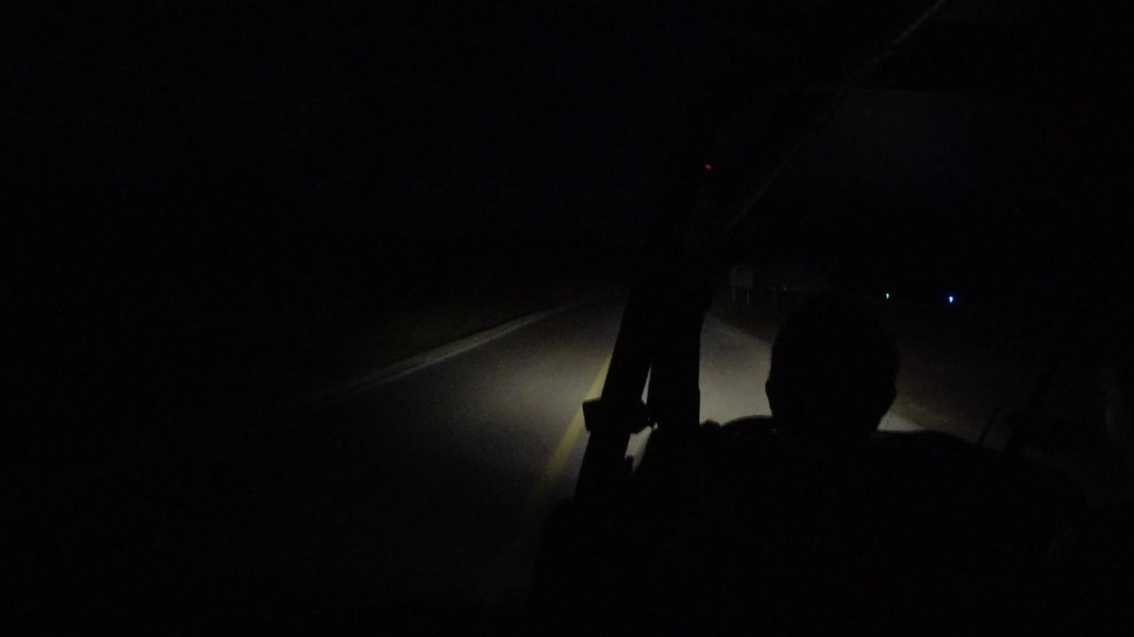 Dark car interior with a silhouetted occupant and headlight beam on the road