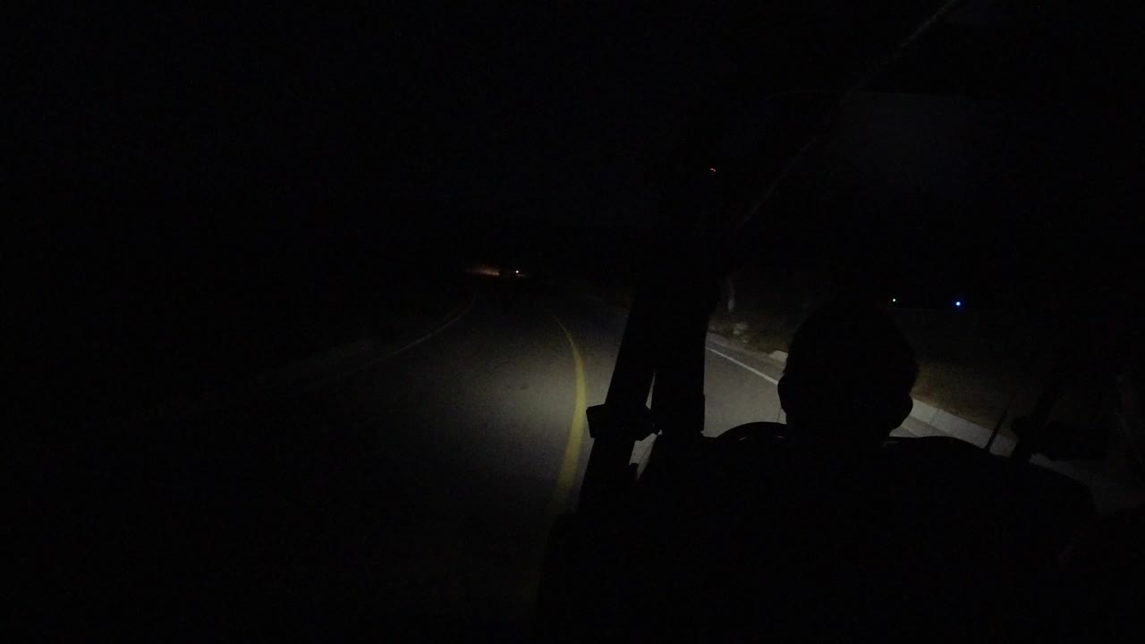 Dark road at night with lane markings lit by headlights.