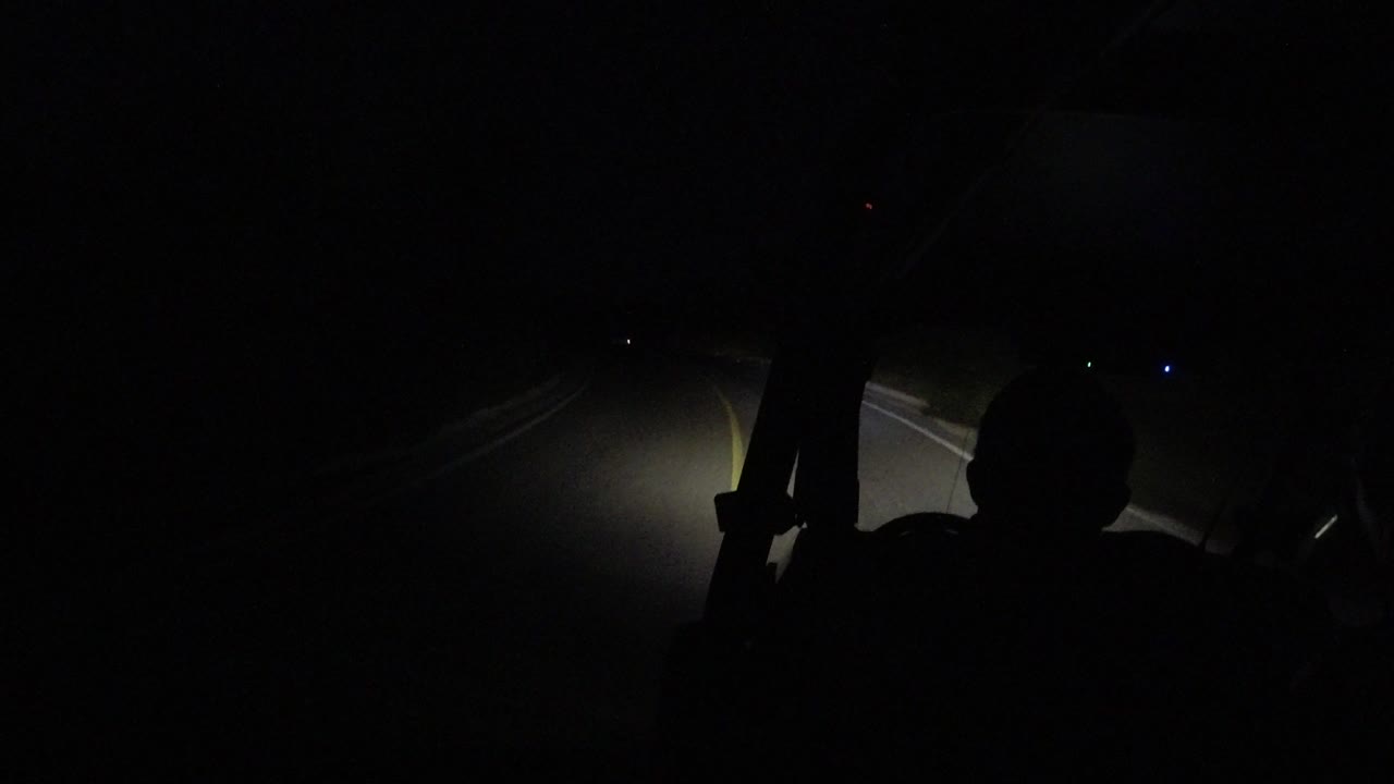The rider remains a dark foreground silhouette while the headlights pick out a yellow stripe and pale pavement edge on the road in Los Cabos, Mexico.