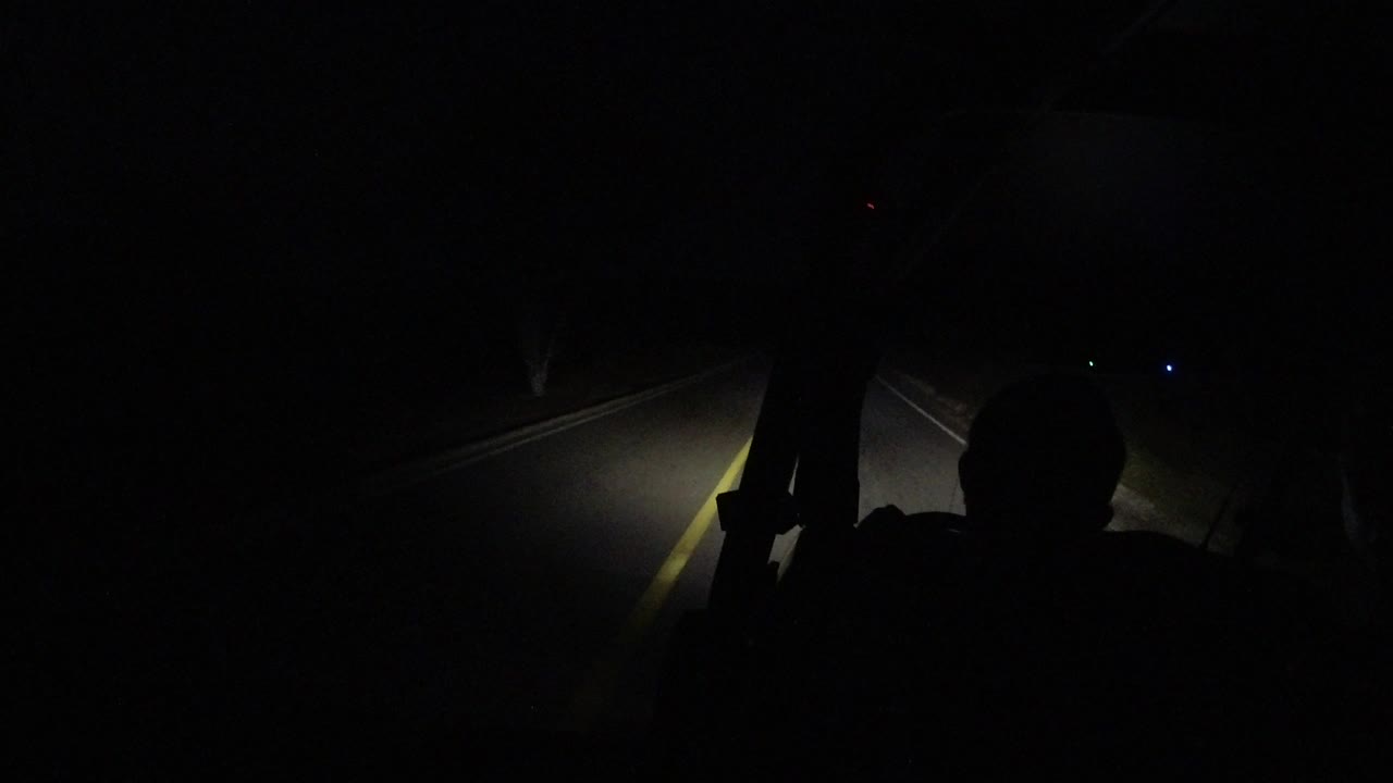 One second in, the headlights catch the edge of a curving road in Los Cabos while a dark interior silhouette remains in the foreground, with no recognizable people visible.