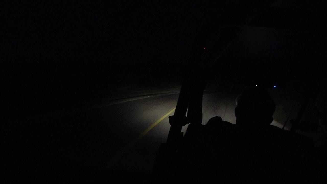 At the start of the Los Cabos night bus clip, a dark interior silhouette frames a road ahead with headlight spill and a yellow center line visible.