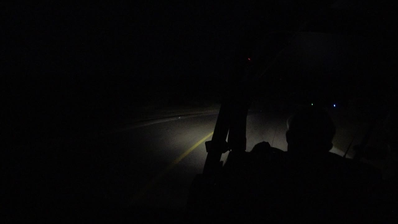 One second in, the Los Cabos road remains mostly black with the windshield edge, a central foreground silhouette, and a short stretch of lane markings lit ahead.