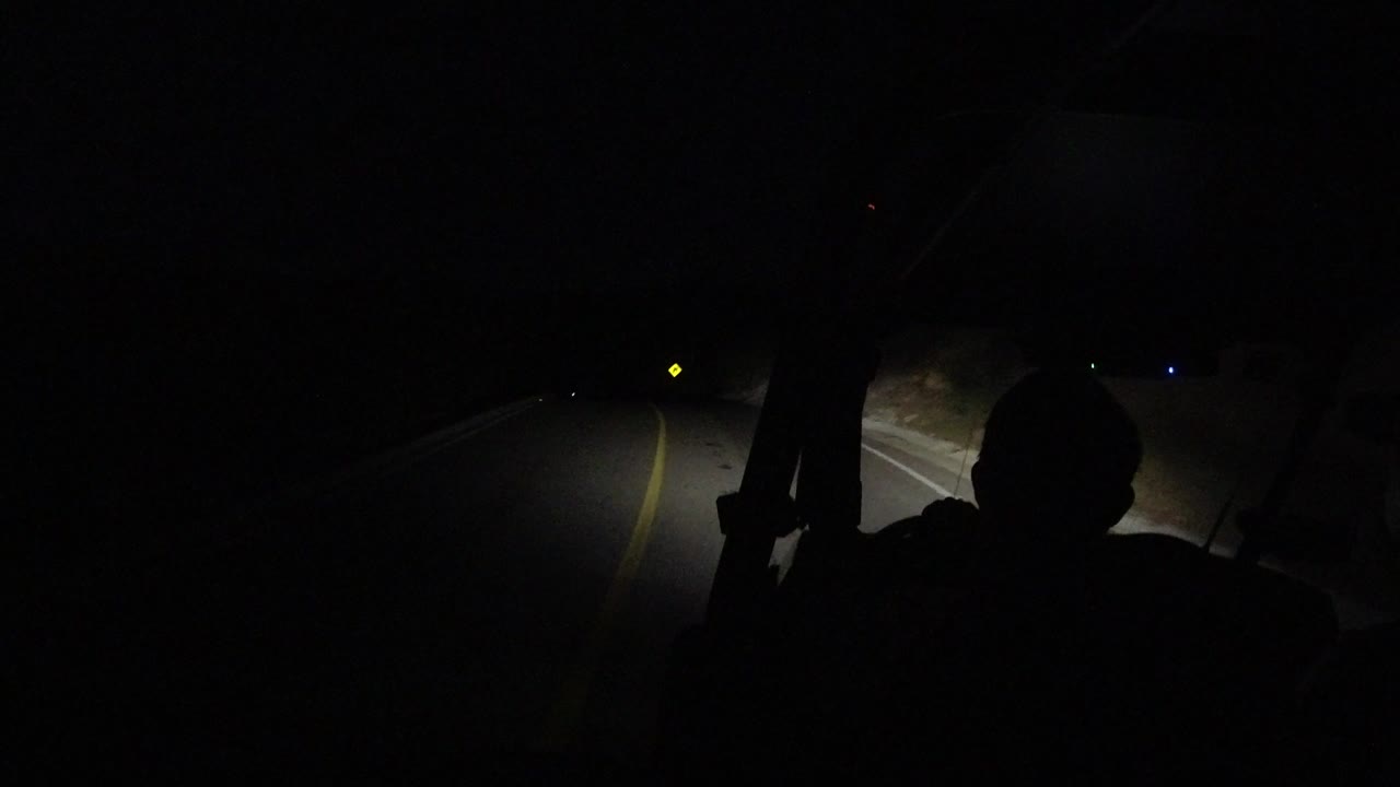 Dark vehicle interior with a silhouetted occupant and headlights on a road.