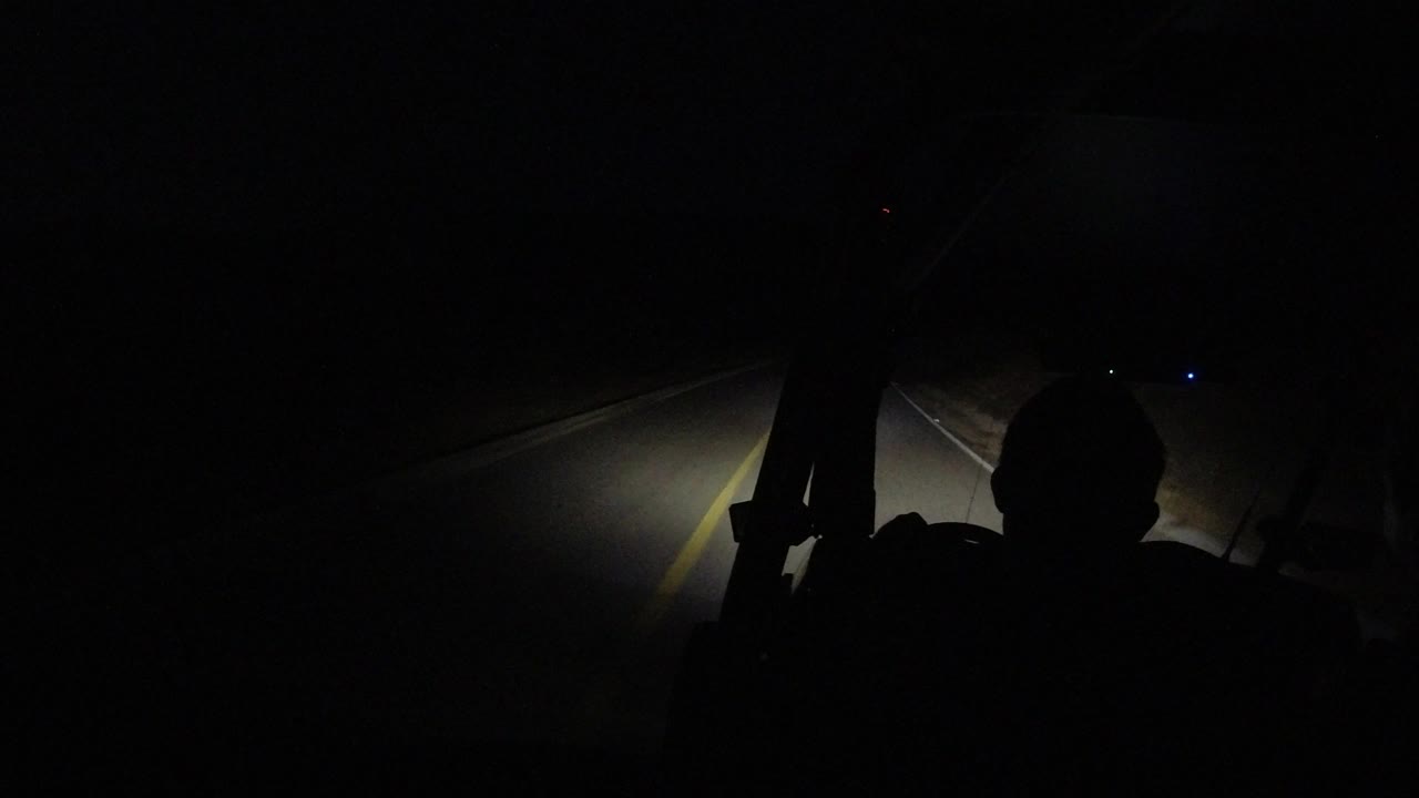 Headlight beam crossing a dark road with interior silhouettes