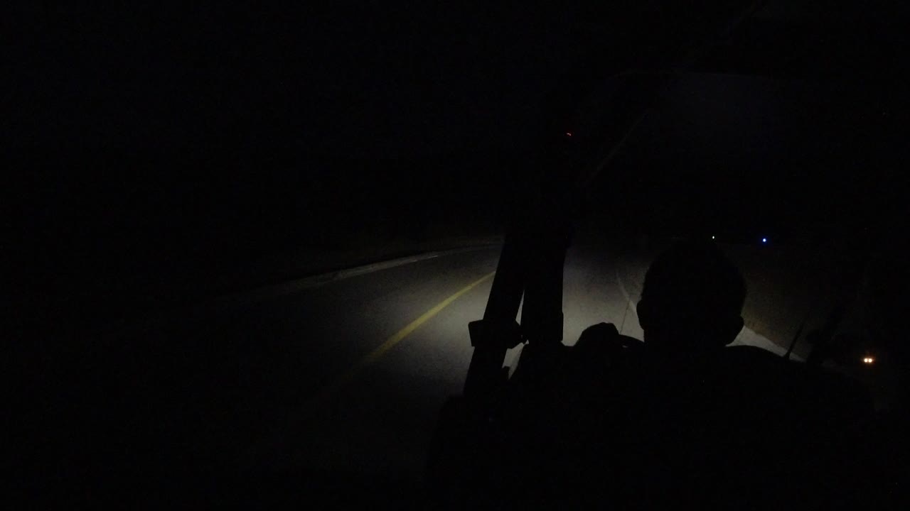 Dark road ahead lit by vehicle headlights with a silhouetted person in the foreground.