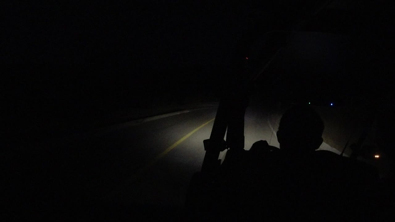 At 0:01 in Los Cabos, Mexico, the headlight beam falls across the road edge as the silhouetted head and shoulders remain visible against the windshield darkness.