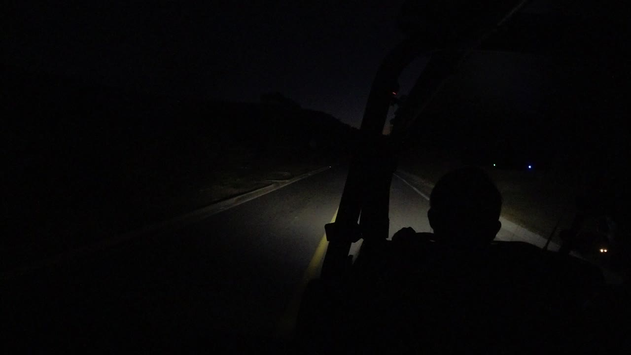 Opening frame in Los Cabos, Mexico showing a silhouetted driver in the foreground as headlights catch the road edge and darkness fills the roadside.