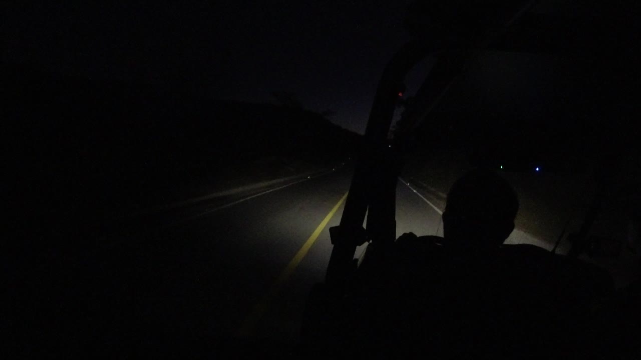 At 0:01 in Los Cabos, Mexico, the headlight beam reaches farther down the lane as the foreground silhouette remains dark and unrecognizable.