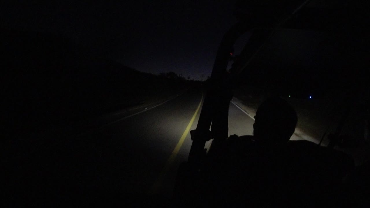 At 0:00 in Los Cabos, Mexico, headlights illuminate a dark road and lane lines while a non-identifiable occupant silhouette sits in the foreground.