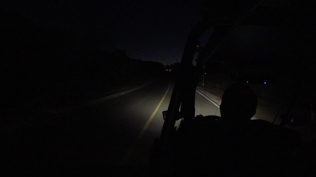 One second in, the Los Cabos night road remains centered beyond the windshield, with a yellow line and a front-seat silhouette in the foreground.