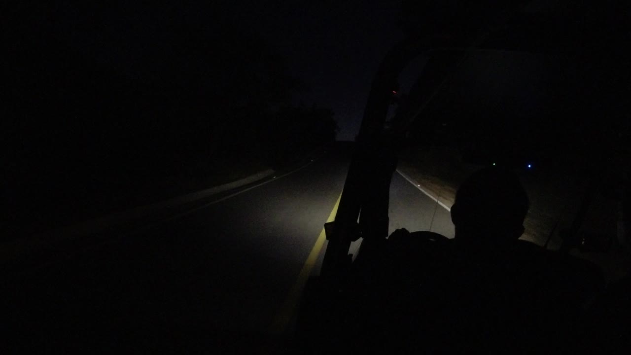 At 0:01, the driver remains in silhouette while the headlight beam reaches farther down a mostly unlit Los Cabos road.