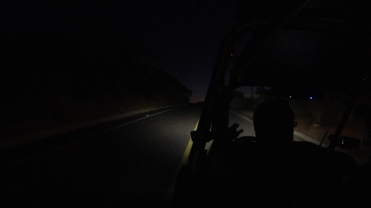 One second in, the driver's dark profile remains in the foreground as the headlights reveal a narrow road edge in Los Cabos, Mexico.
