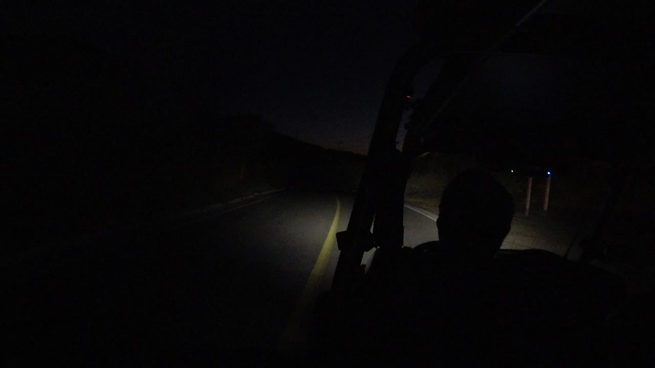 At the start of the Los Cabos clip, a driver silhouette sits in the foreground while the bus headlights pick out a road line and roadside edge in the darkness.