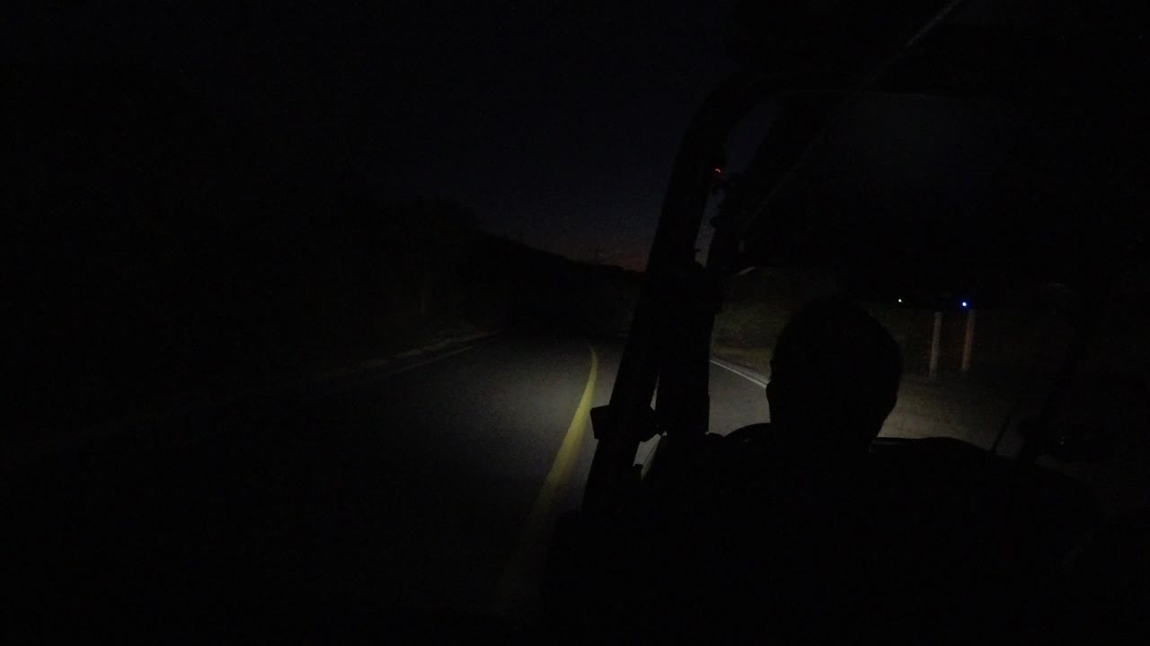 One second in, the Los Cabos bus driver remains silhouetted as the headlight beam falls across the lane line and a dark roadside shoulder.