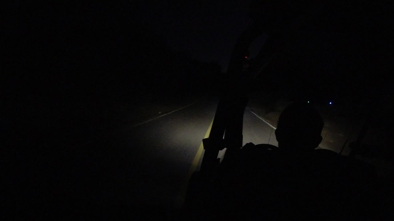 Dark road at night with headlight beam and seated silhouette