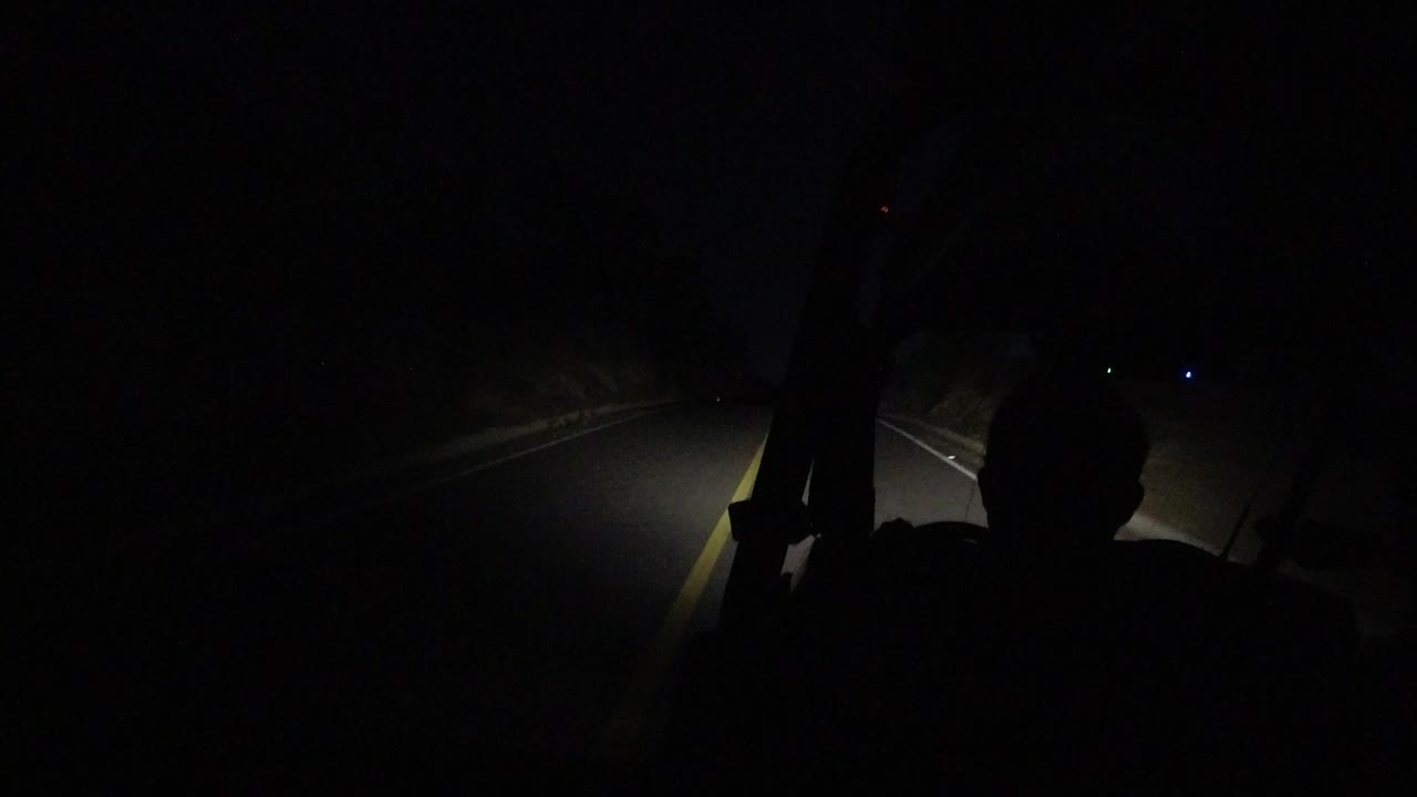 Driver silhouette inside a dark vehicle with headlights on a road