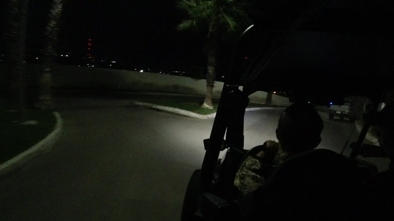 The Jeep view in Los Cabos shows headlights sweeping across a curb, grass strip, palm trunk, and low wall, with a passenger silhouette at right.
