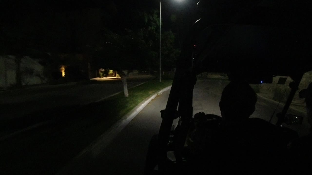 A second nighttime frame shows the same vehicle foreground, silhouetted riders, a narrow lit strip of road, trees on both sides, and small distant lights in Los Cabos.