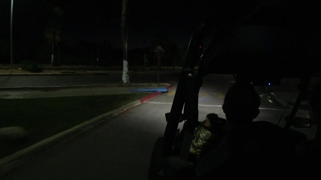 Los Cabos night road view from behind the driver, with the vehicle frame in shadow and a narrow pool of light on the pavement ahead.