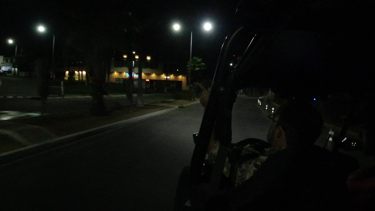 Night road seen from a dune buggy with silhouetted riders and lit shops ahead.