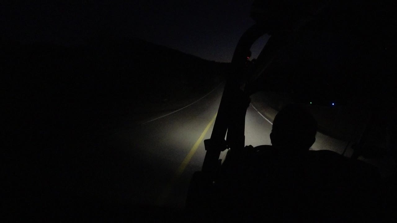 A Los Cabos night road view from the buggy shows the foreground rider in shadow and the headlight beam widening across the lane line.