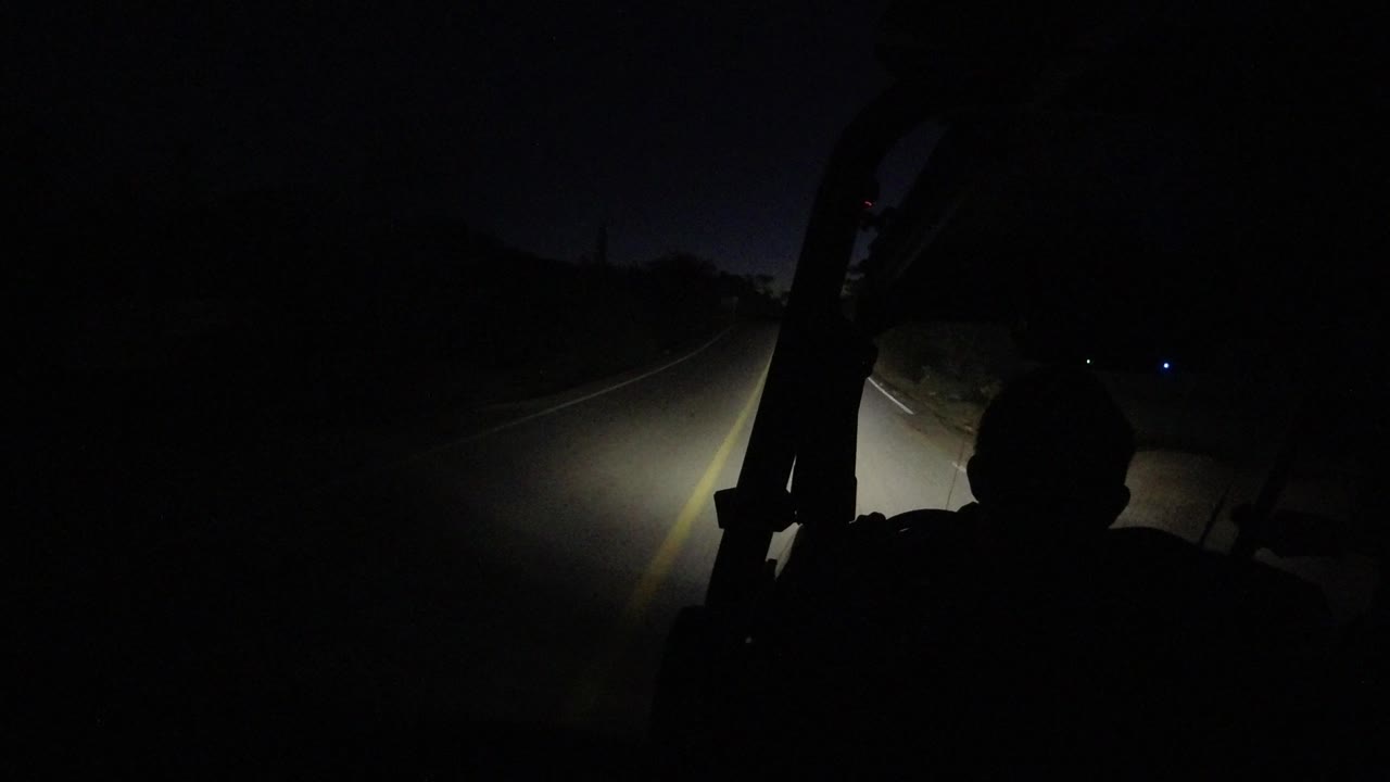 Night road ahead with headlight beam and dark foreground silhouette.