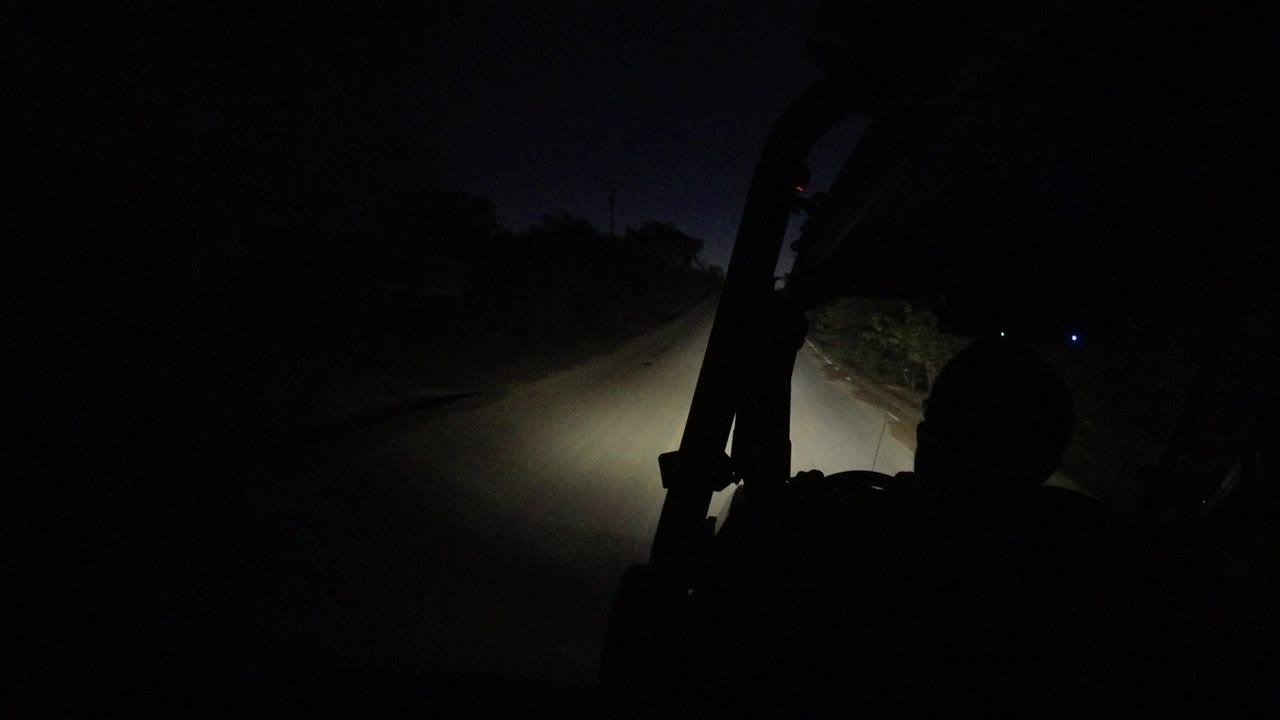 Dark road lit by vehicle headlights with a passenger silhouette in the foreground.
