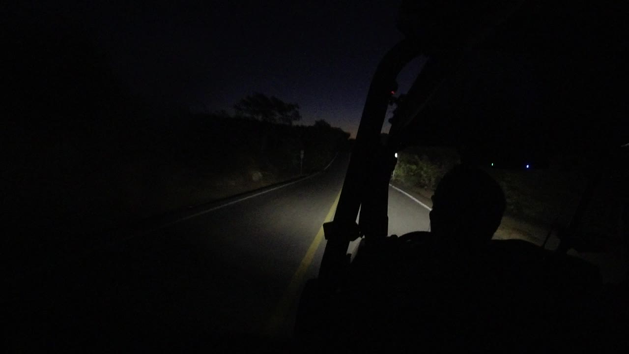 Night driving view with headlight wash, road lines, and a dark foreground silhouette.