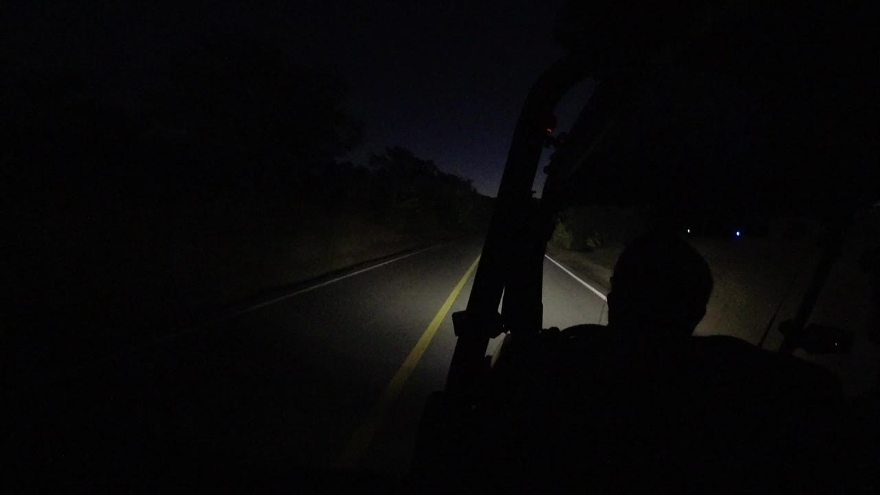 Dark road seen from inside a vehicle with headlights on.