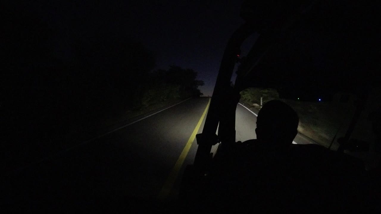 Dark vehicle interior facing an empty road lit by headlights.