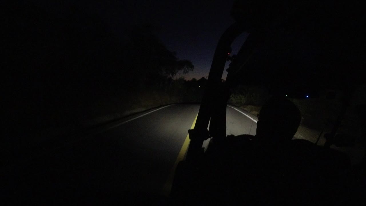 Dark road seen by headlights with a seated silhouette at right.