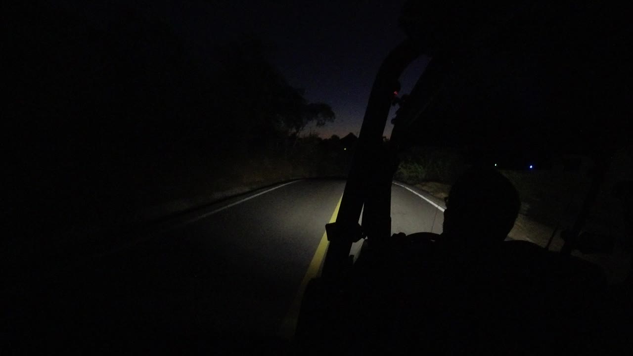 A later moment in the Los Cabos night drive shows the road bending gently, with the passenger silhouette darker against the headlight wash.
