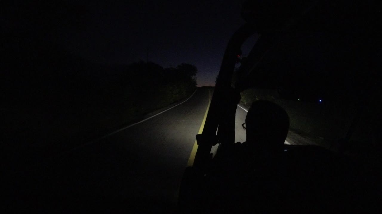 Dark road lit by headlights with a driver silhouette inside a Jeep.