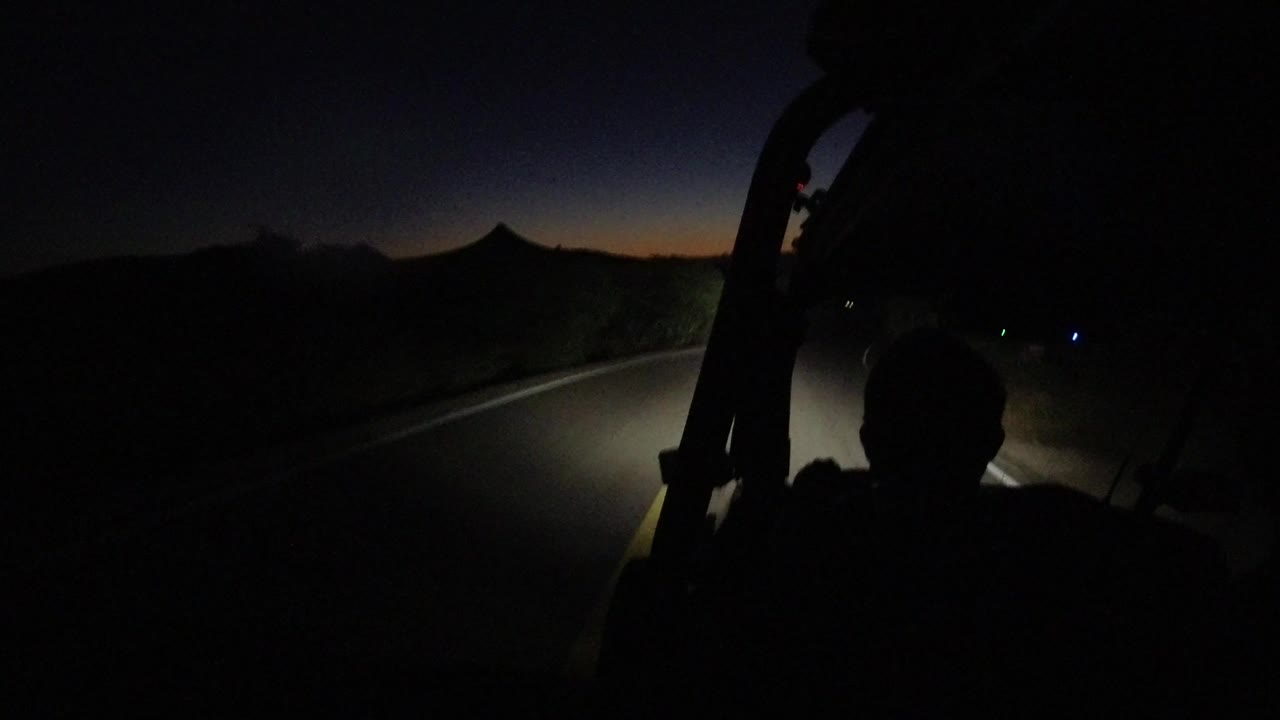 Dark jeep road view with headlights on pavement at dusk.