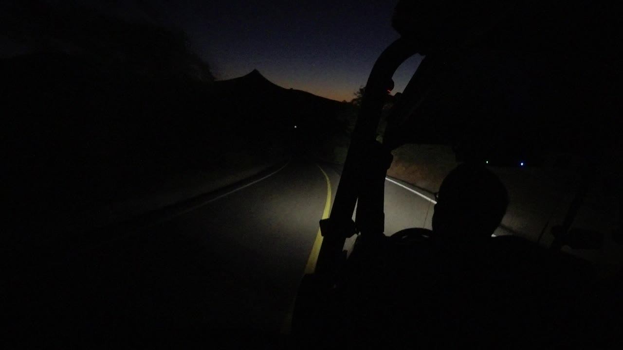 The Los Cabos night road bends through darkness while the buggy's headlight beam catches the lane markings and the rider remains in silhouette.