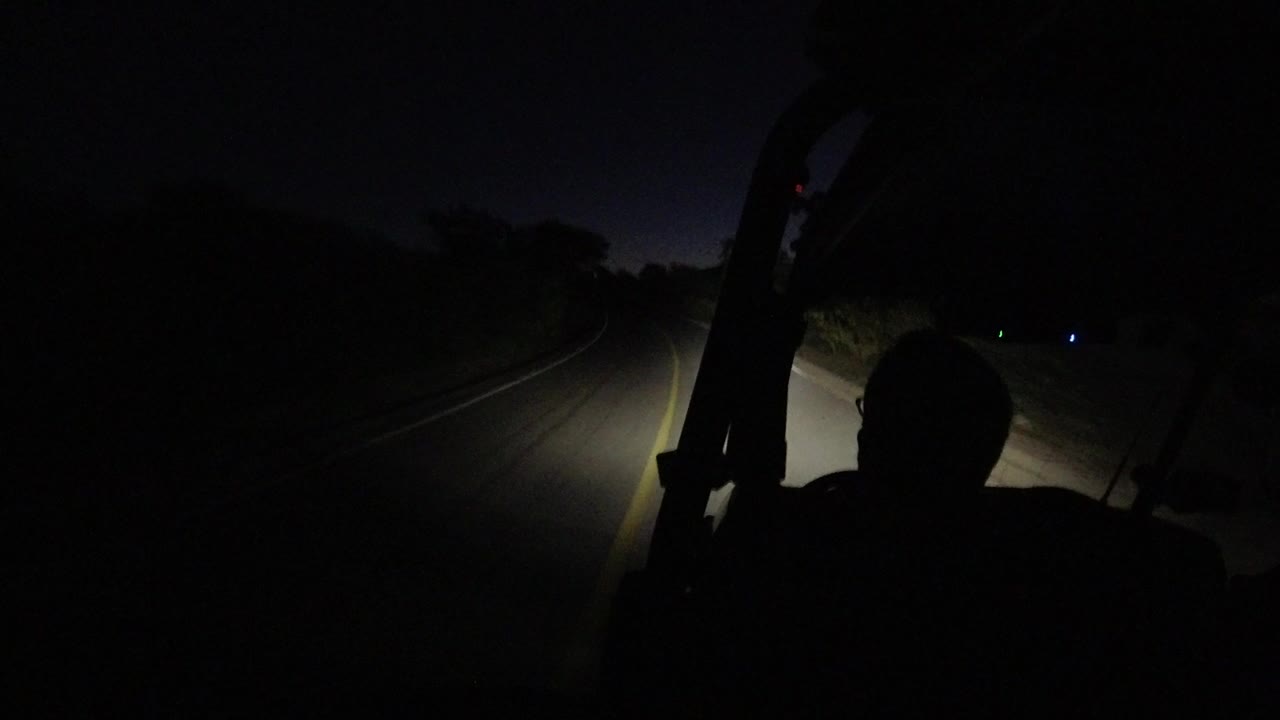 Dark road lit by headlights with a foreground human silhouette.