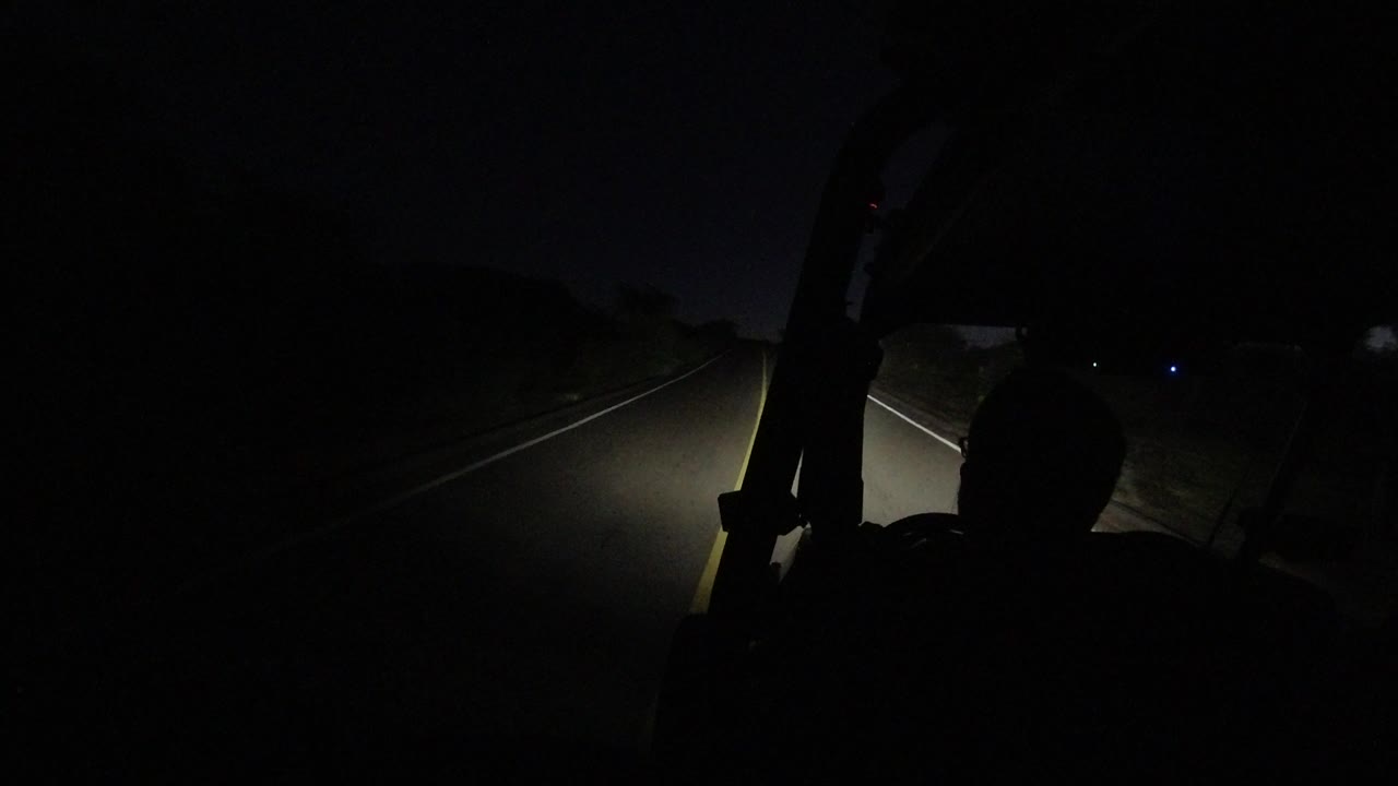 At 0:01 in Los Cabos, Mexico, the jeep moves through darkness with the driver's head silhouetted against a narrow headlight beam on the road.