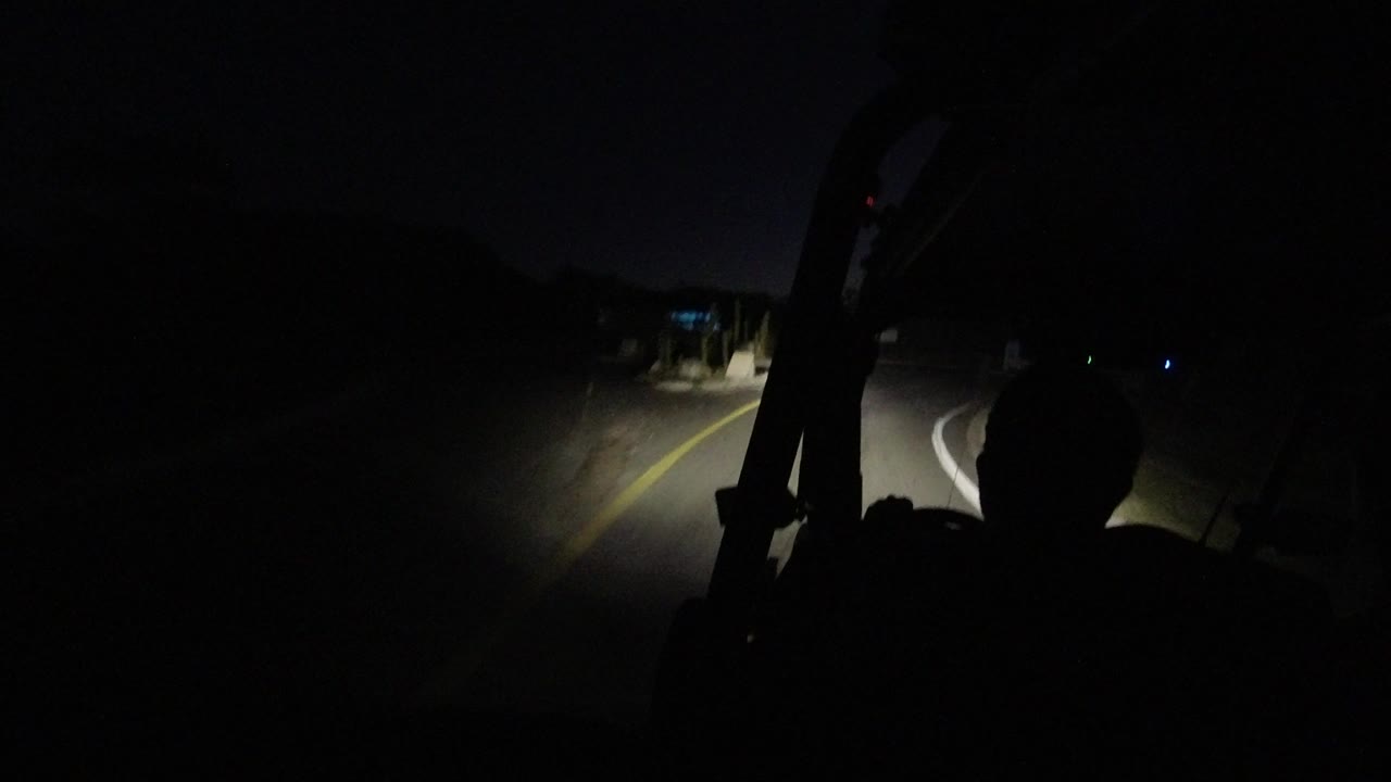 At 0:01 in Los Cabos, Mexico, the Jeep headlights reach a curving section of road with yellow lane paint, low roadside edges, and a dark passenger silhouette.