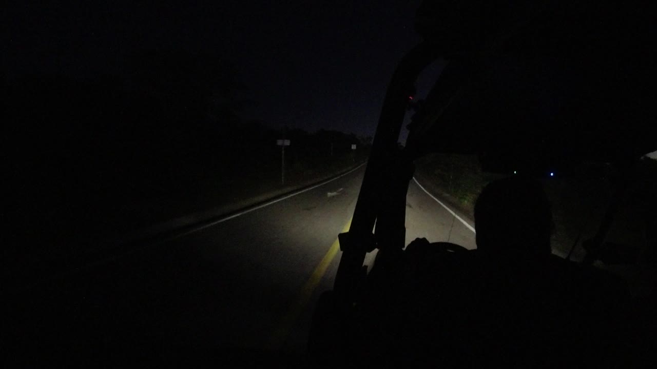 Headlights reveal a highway lane and roadside sign in darkness.