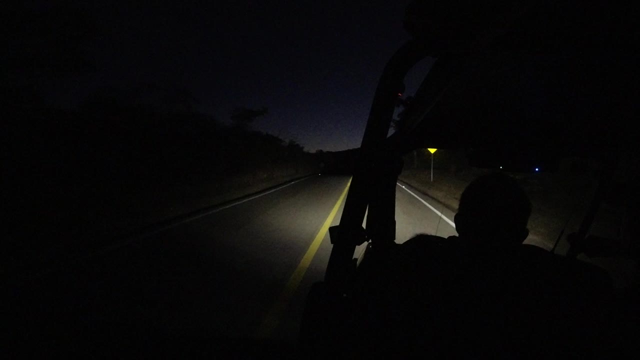 Night road lit by vehicle headlights with dark foreground silhouettes.