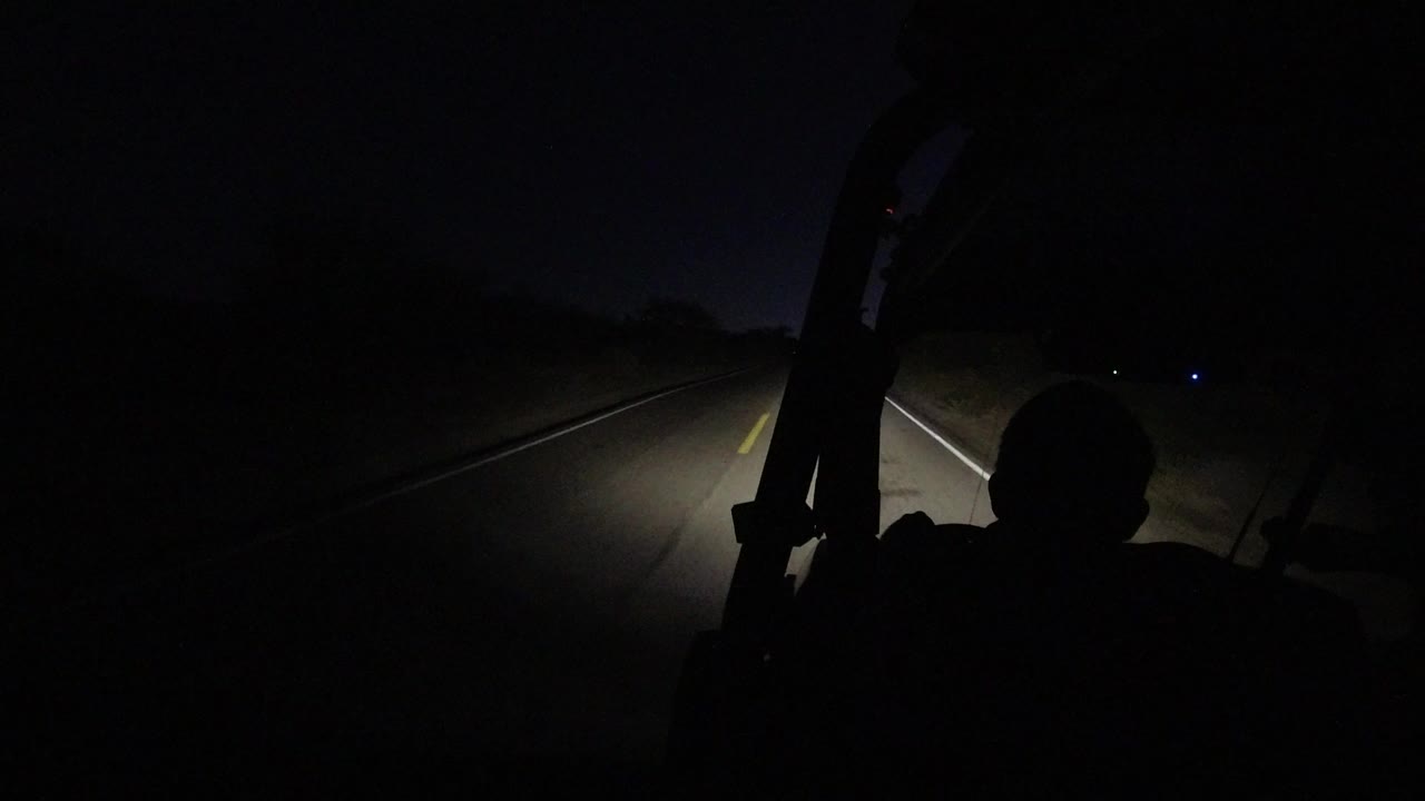 Start of a dark Los Cabos road view, with headlights revealing lane markings and roadside brush while no identifiable people are visible.