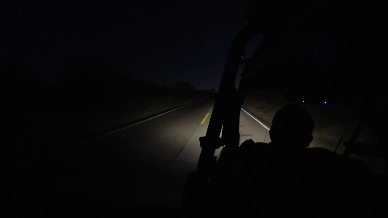 A second of the Los Cabos nighttime road, with the headlight beam falling slightly right of center and a dark foreground silhouette at the lower right.
