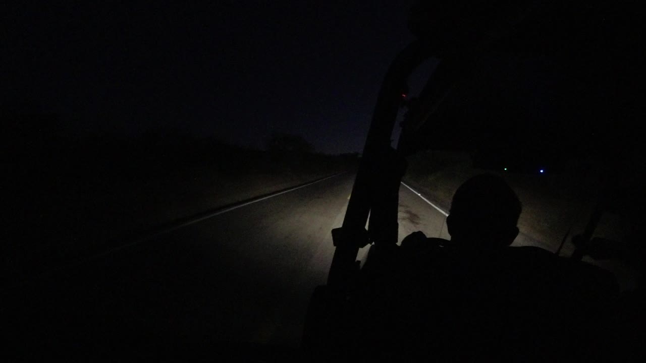 Los Cabos highway pavement and lane lines appear under dim headlights, with most of the frame falling into darkness and no identifiable people visible.