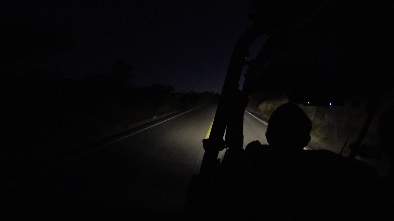 At the start of the Los Cabos night drive, headlights illuminate the lane ahead while a dark human silhouette sits in the foreground.