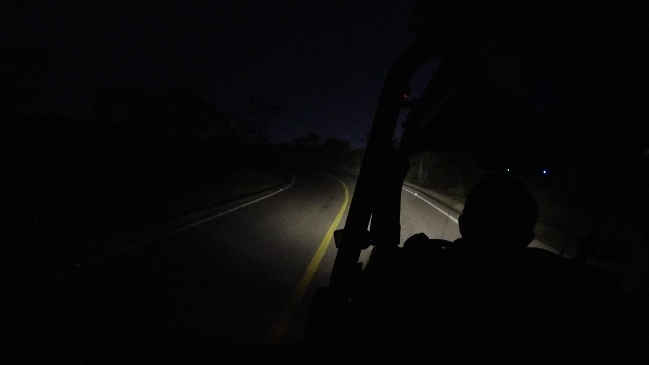 Dark road ahead lit by headlights with a passenger silhouette at right.